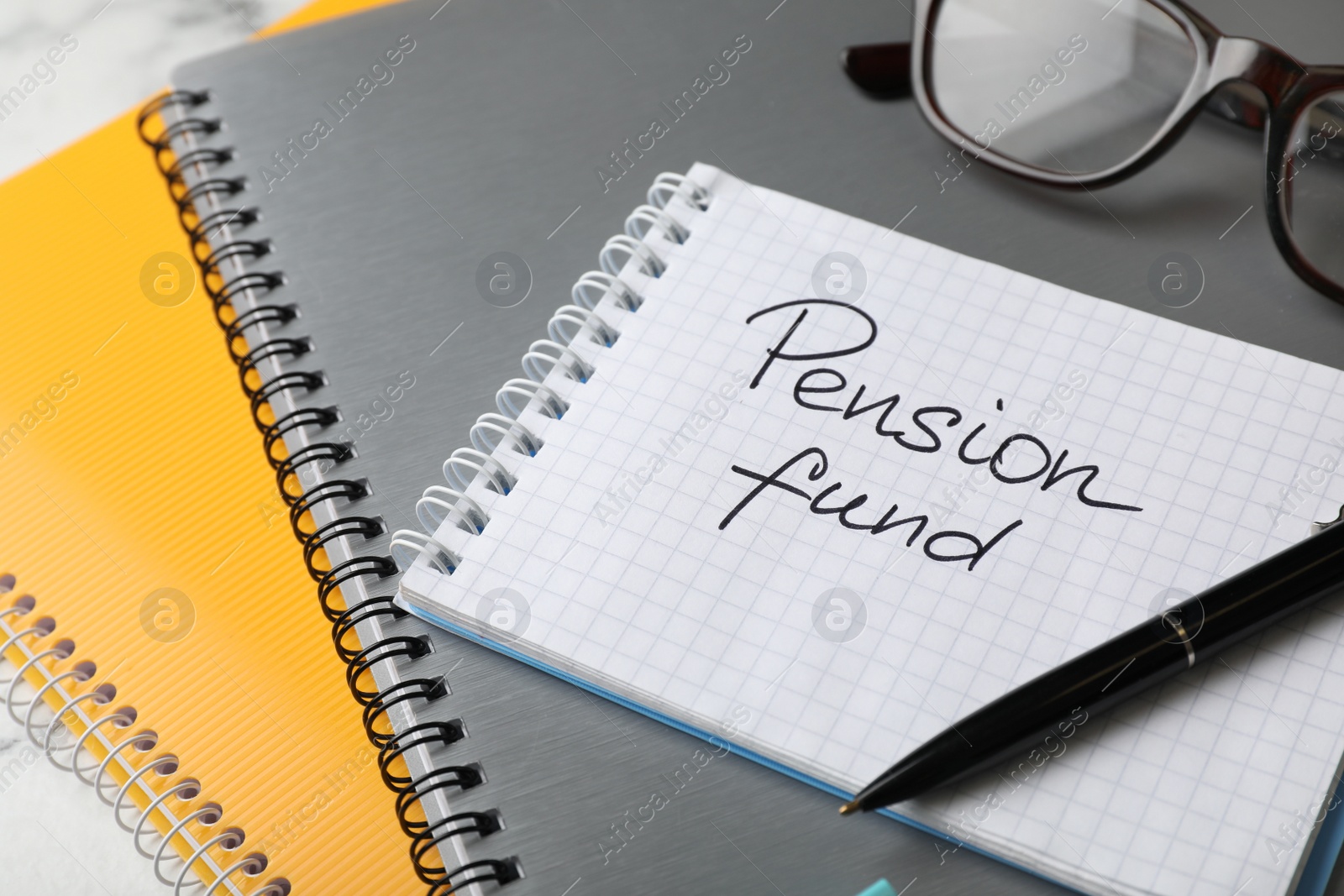 Photo of Glasses and notebook with words PENSION FUND on table