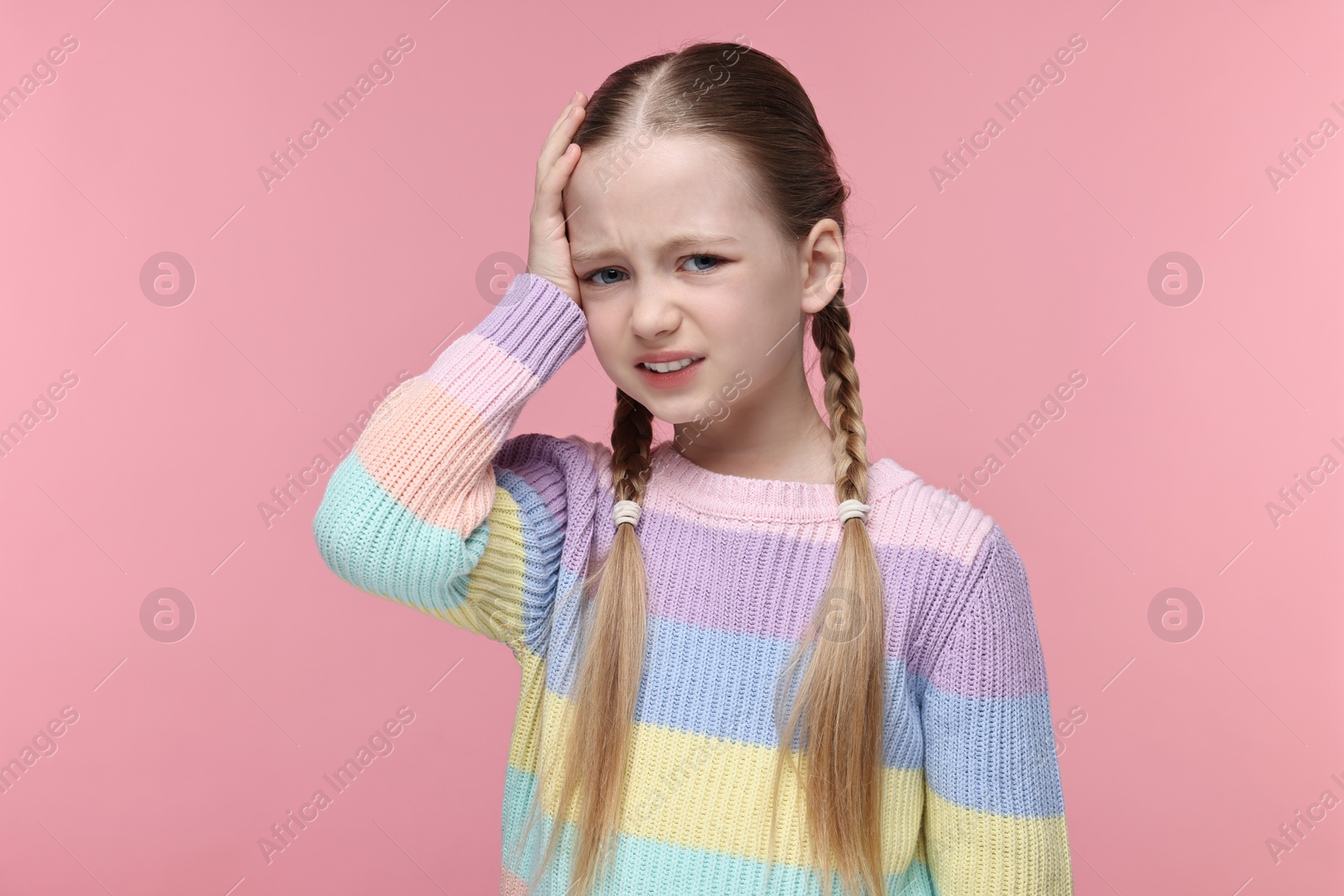 Photo of Little girl suffering from headache on pink background