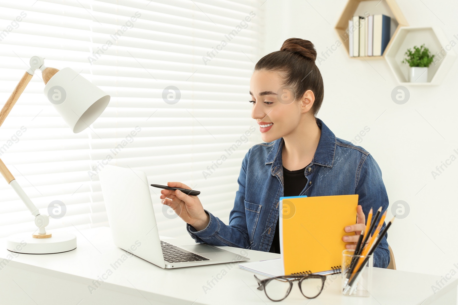 Photo of Home workplace. Happy woman working on laptop at white desk in room