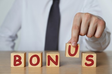 Image of Man making word Bonus of cubes with letters on wooden table, closeup