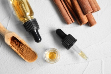 Photo of Bottles of essential oils, cinnamon sticks and powder on white table, flat lay