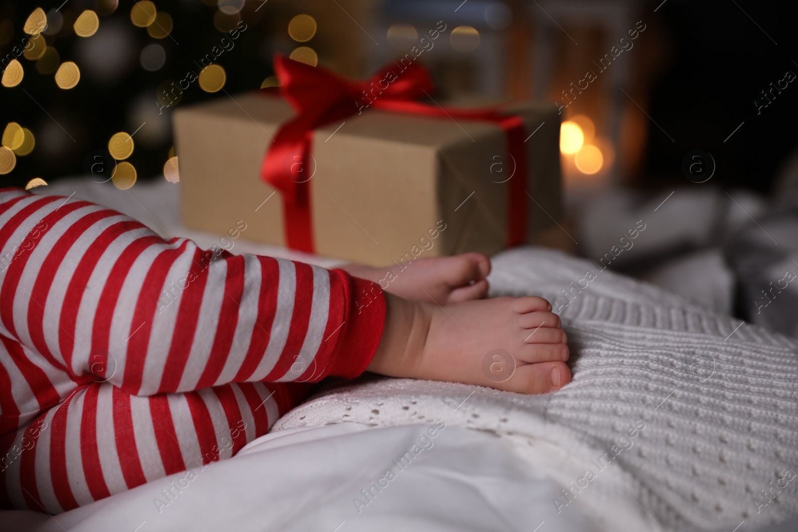 Photo of Baby in Christmas pajamas sleeping near gift box on bed indoors, closeup