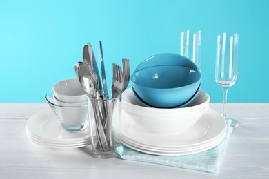 Set of clean dishes, glasses and cutlery on table against color background