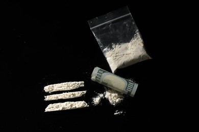 Photo of Drug addiction. Plastic bag with cocaine and rolled dollar banknote on black background,, flat lay