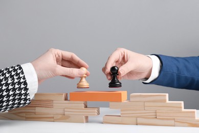 Photo of Businesspeople putting pawns on bridge made of wooden blocks at table, closeup. Connection, relationships and deal concept