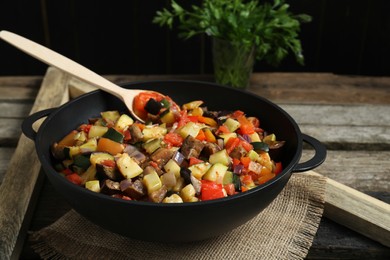 Photo of Delicious ratatouille and spoon in baking dish on wooden table, closeup