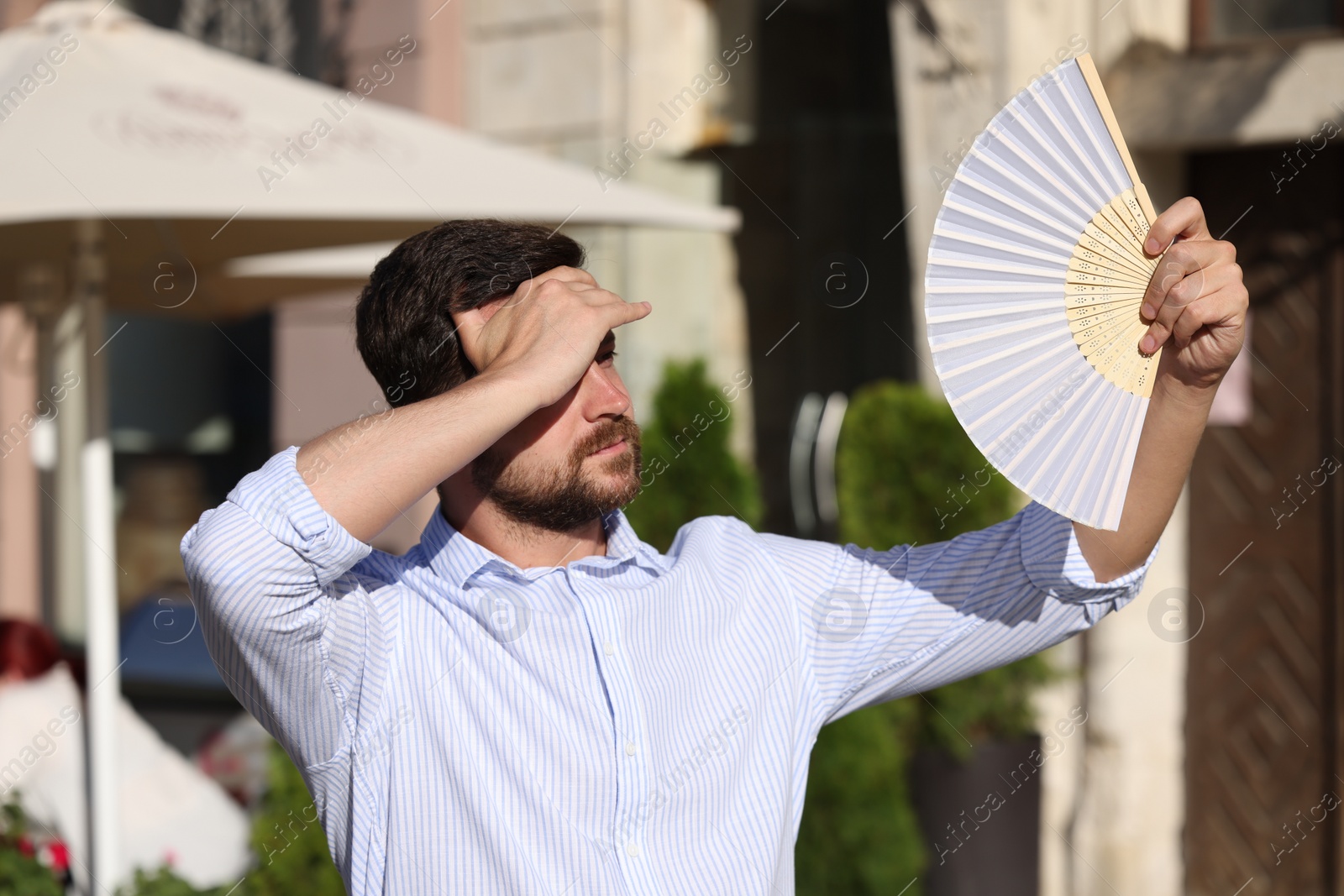 Photo of Man with hand fan suffering from heat outdoors