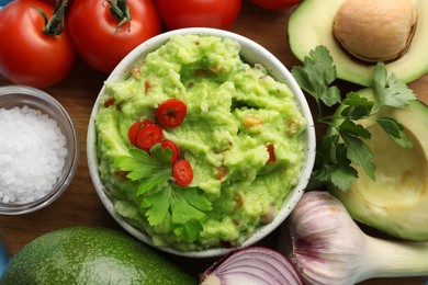 Photo of Delicious guacamole and ingredients on wooden table, flat lay