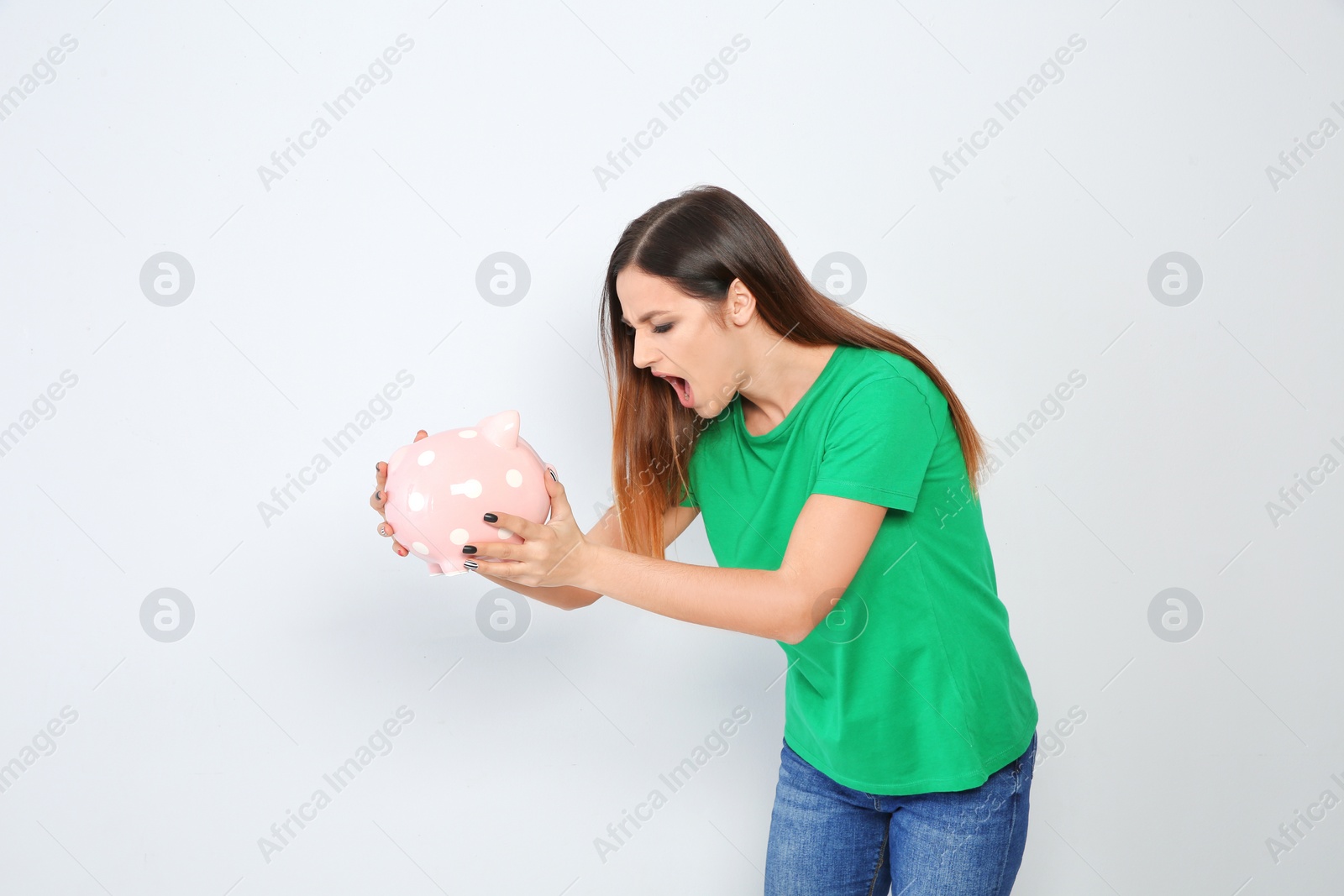 Photo of Emotional young woman with piggy bank on white background