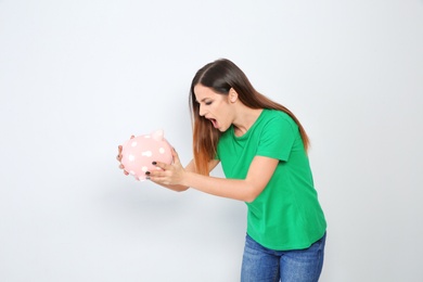 Emotional young woman with piggy bank on white background