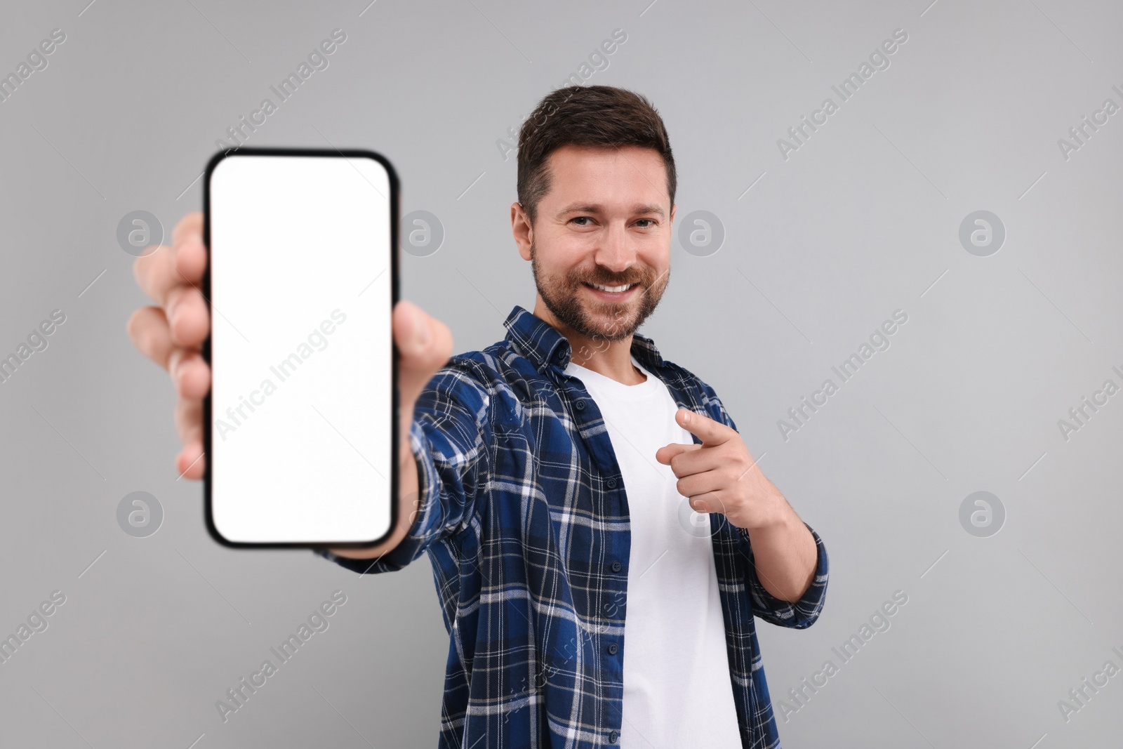 Photo of Handsome man showing smartphone in hand and pointing at it on light grey background