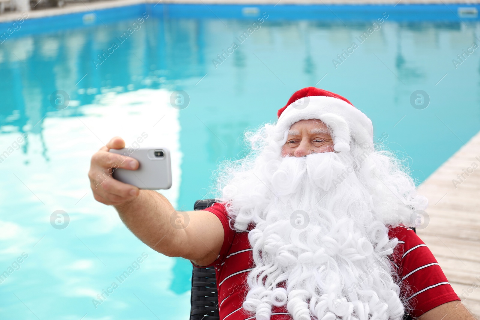 Photo of Authentic Santa Claus taking selfie near swimming pool outdoors