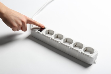 Photo of Woman pressing power button of extension cord on white background, closeup. Electrician's equipment