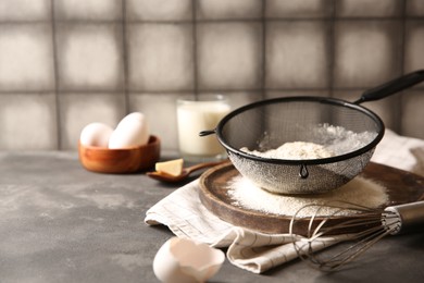 Flour in sieve and other ingredients for dough on grey textured table, closeup. Space for text