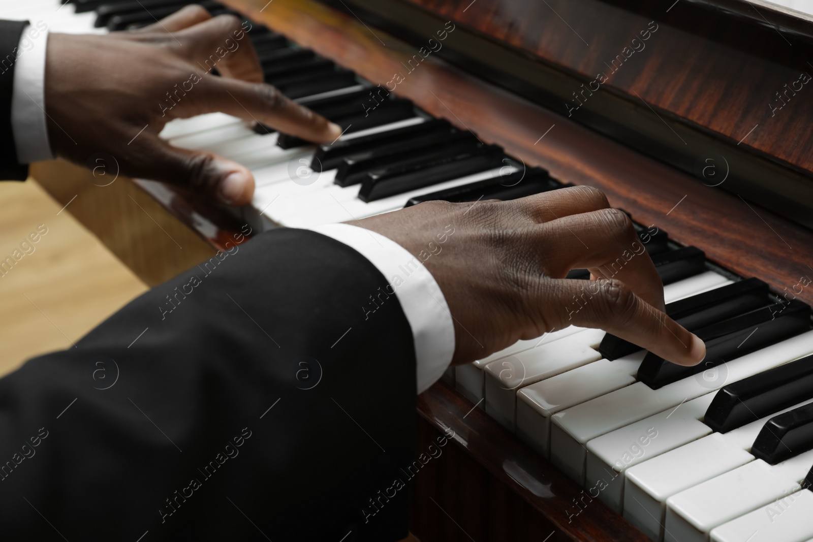 Photo of African-American man playing piano indoors, closeup. Talented musician