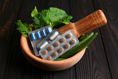 Photo of Mortar with fresh green herbs and pills on wooden table
