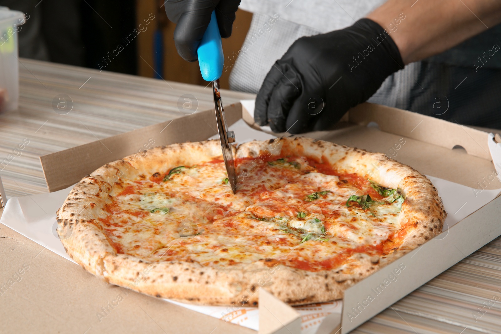 Photo of Professional chef cutting Italian oven baked pizza on table in restaurant, closeup