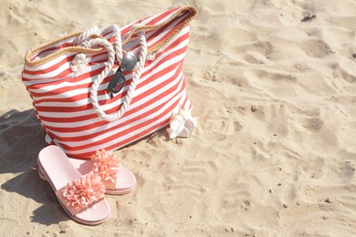 Stylish striped bag with slippers and sunglasses on sandy beach. Space for text