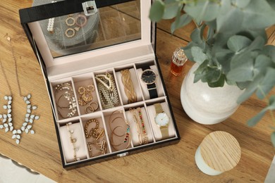 Elegant jewelry box with beautiful bijouterie and expensive wristwatches near luxury perfume on wooden table, flat lay