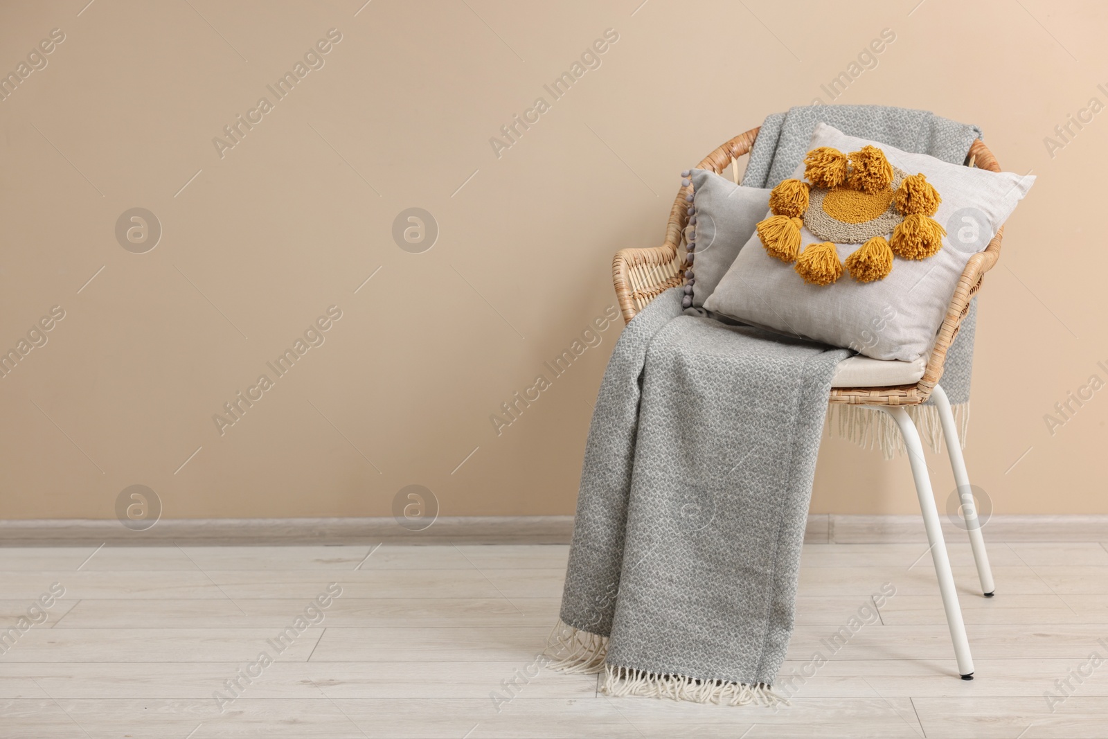 Photo of Stylish soft pillow and blanket on armchair near beige wall indoors. Space for text