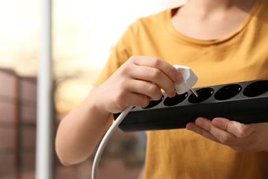 Photo of Woman inserting power plug into extension cord indoors, closeup. Electrician's professional equipment