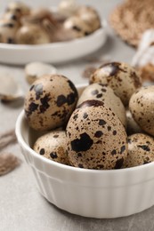 Photo of Fresh quail eggs in bowl on light grey table, closeup