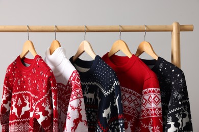 Different Christmas sweaters hanging on rack against light background