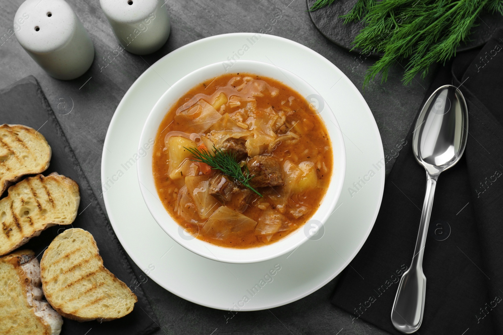 Photo of Tasty cabbage soup with meat, carrot and dill served on black table, flat lay