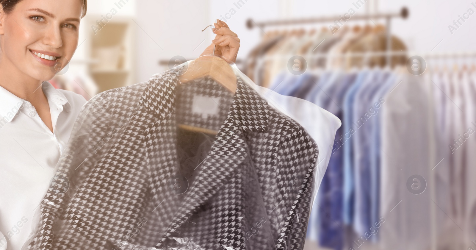 Image of Dry-cleaning service. Happy woman holding hanger with coat in plastic bag indoors, space for text. Banner design