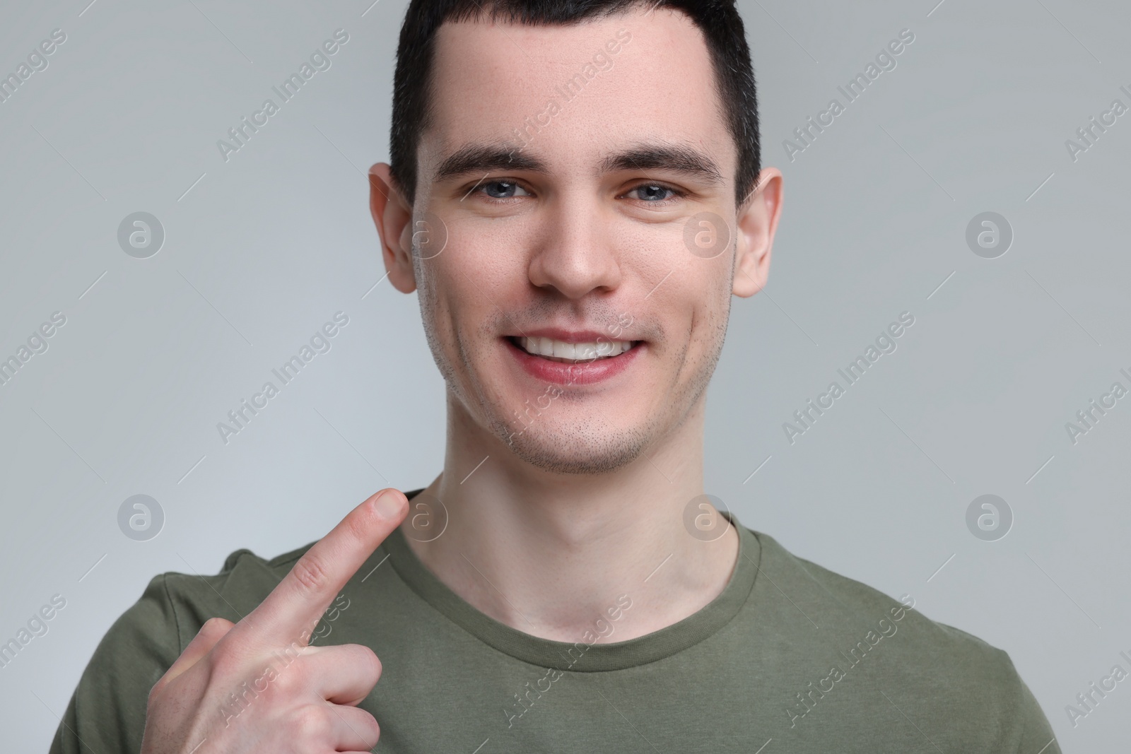 Photo of Young man showing his teeth with whitening strip on light grey background