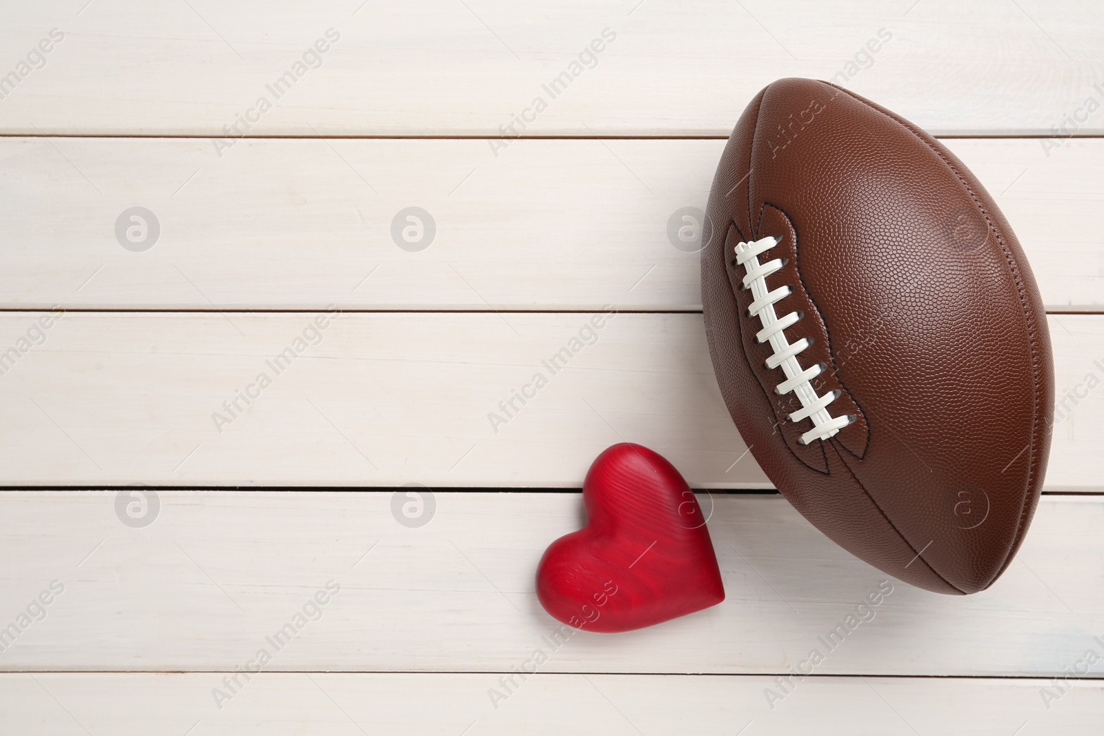 Photo of American football ball and heart on white wooden background, flat lay. Space for text