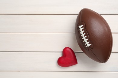 Photo of American football ball and heart on white wooden background, flat lay. Space for text