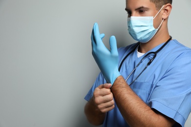 Doctor in protective mask putting on medical gloves against light grey background. Space for text