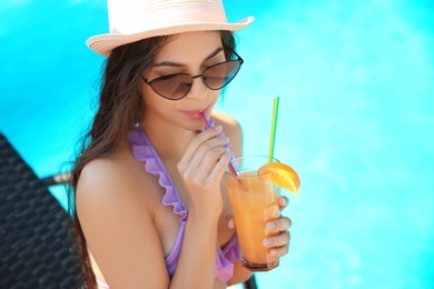 Photo of Beautiful young woman with cocktail in bikini near swimming pool