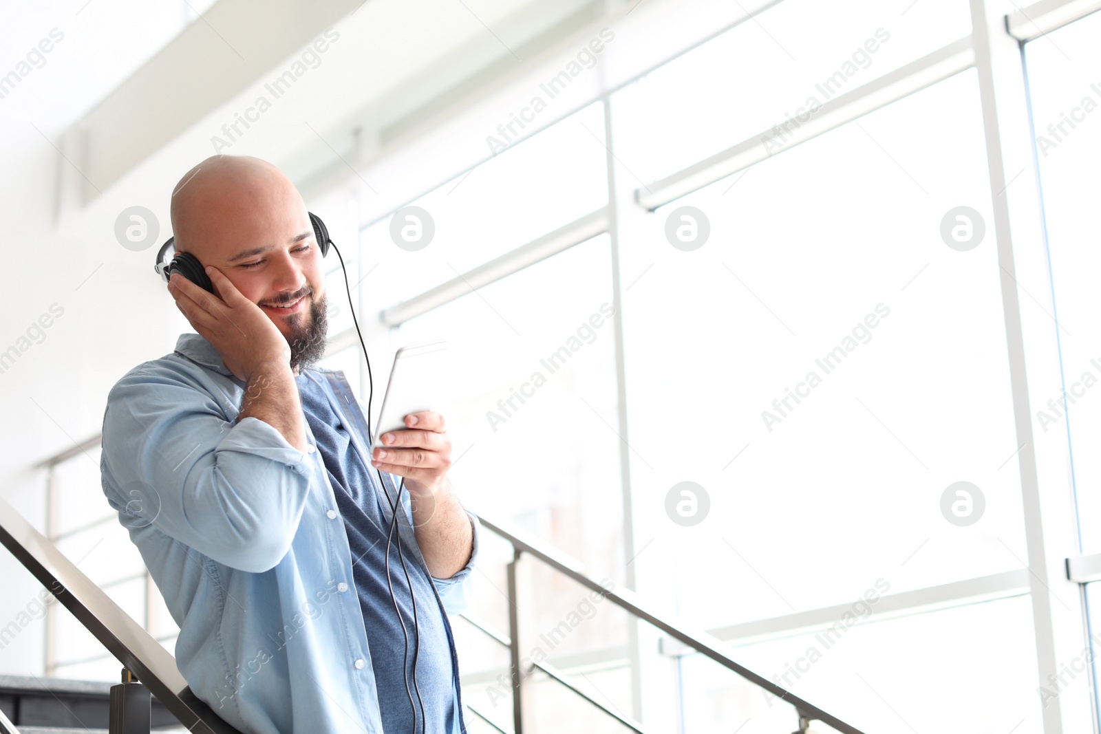 Photo of Portrait of young man with mobile phone and headphones on stairs