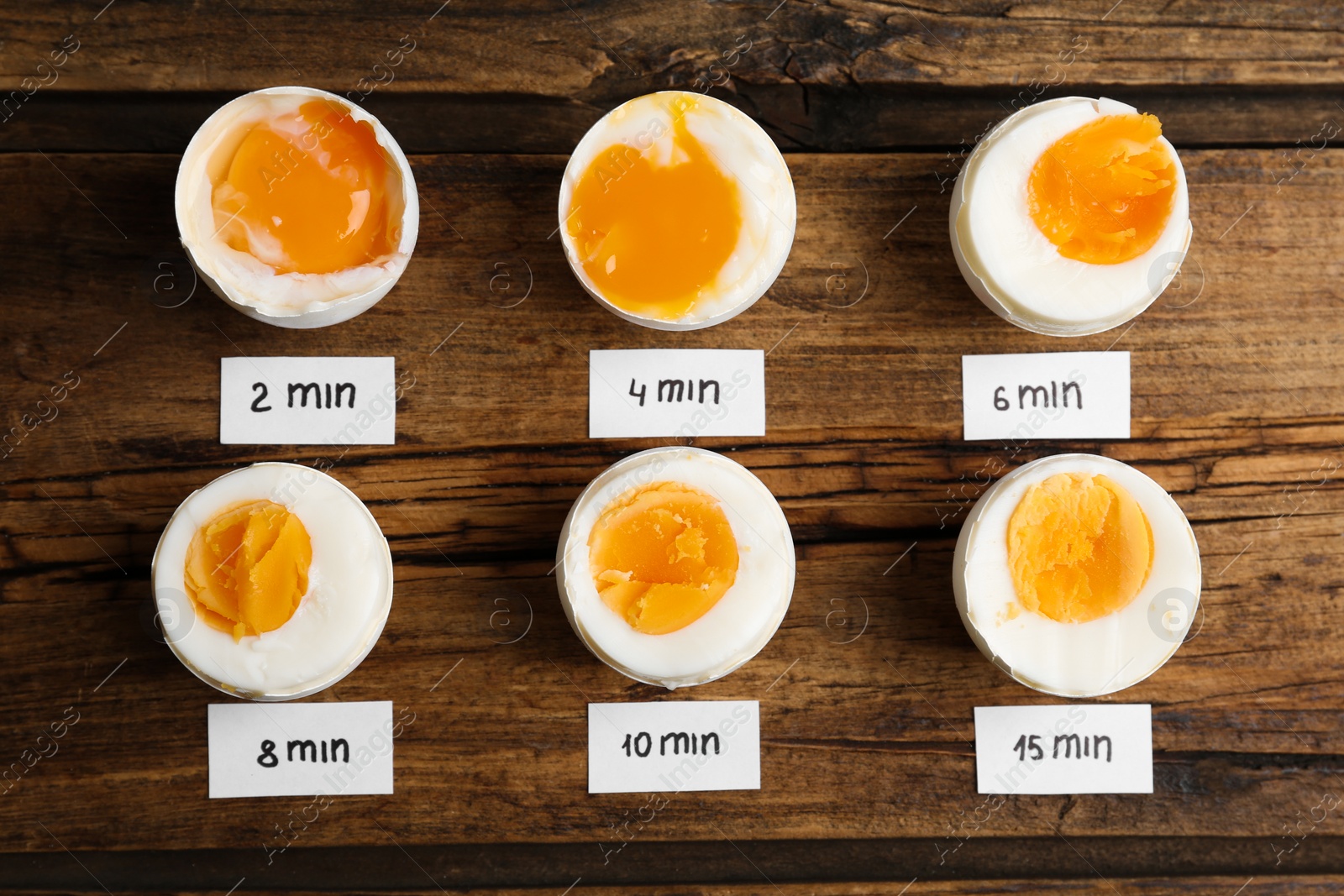 Photo of Different cooking time and readiness stages of boiled chicken eggs on wooden table, flat lay