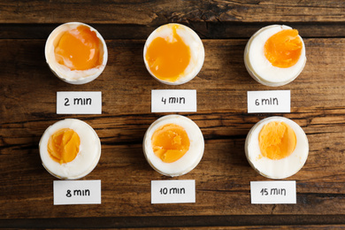 Different cooking time and readiness stages of boiled chicken eggs on wooden table, flat lay