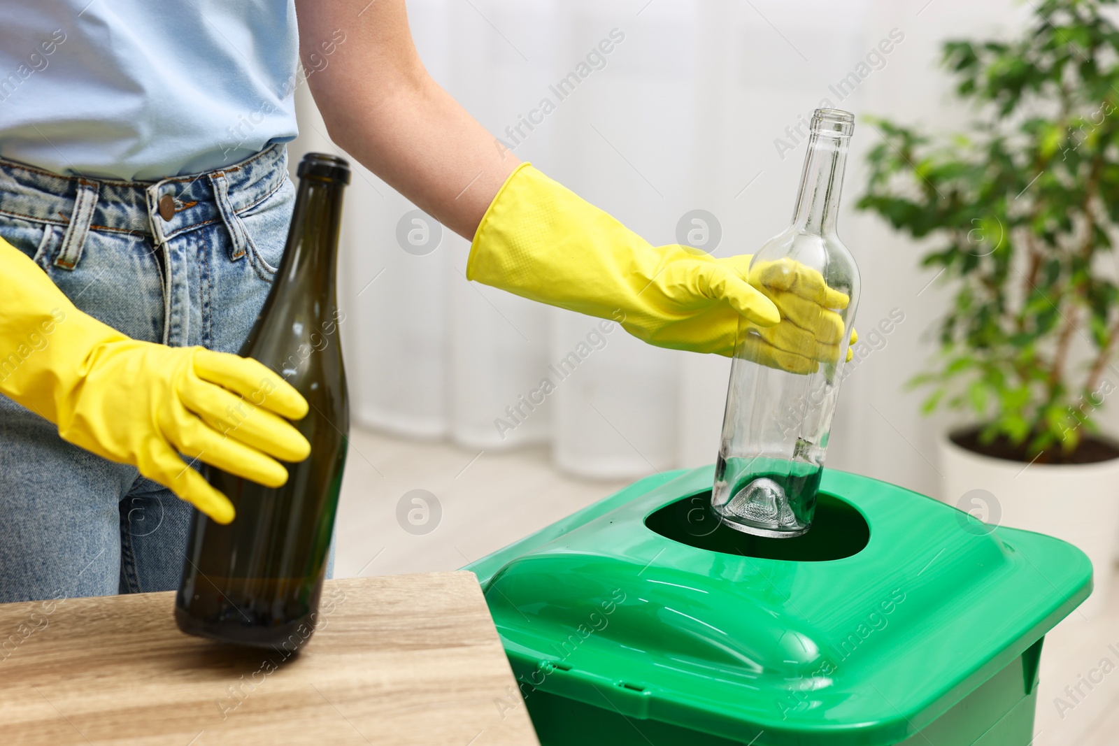 Photo of Garbage sorting. Woman throwing glass bottle into trash bin in room, closeup