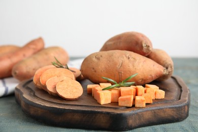 Photo of Wooden board with cut and whole sweet potatoes on light blue table