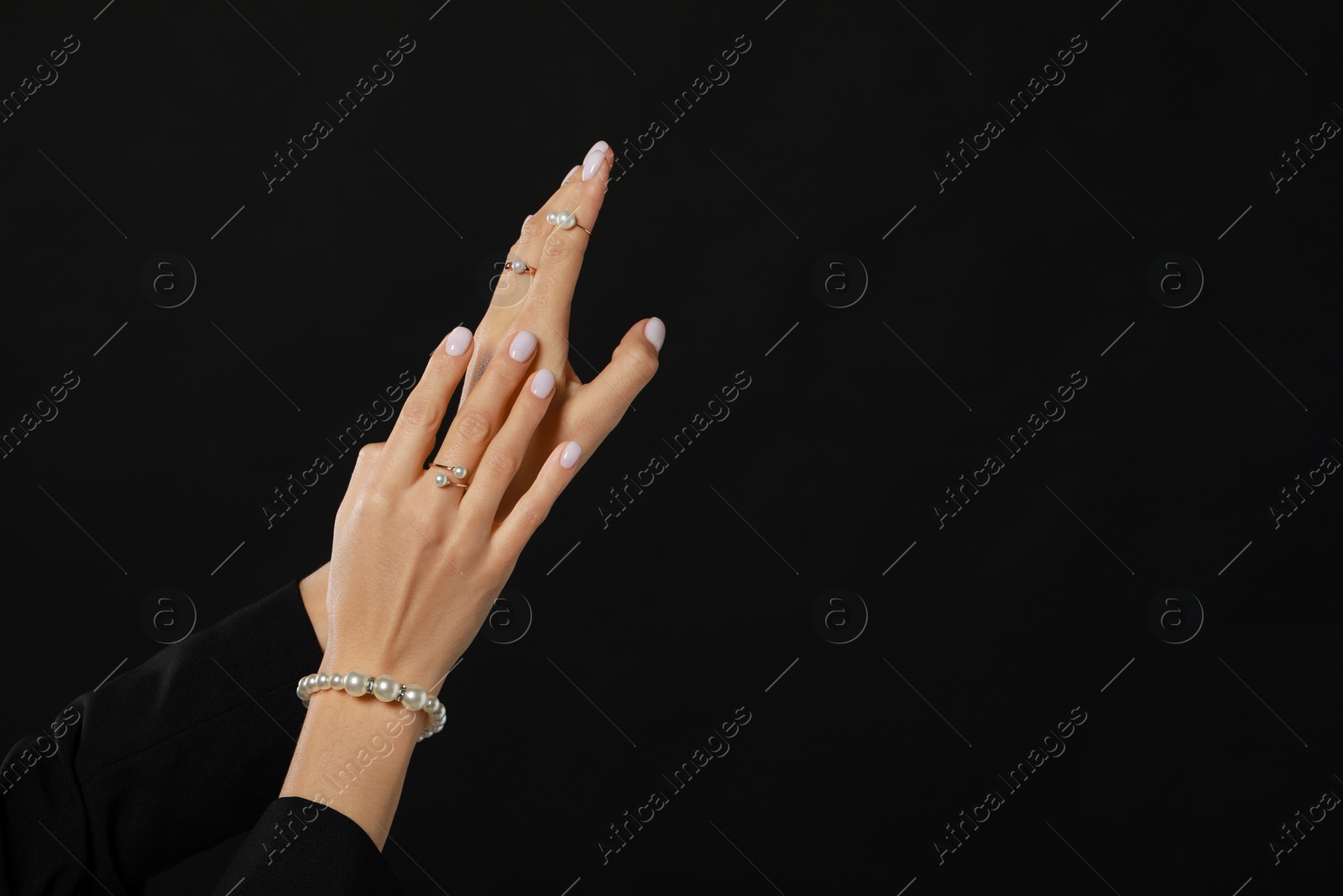 Photo of Young woman with elegant pearl jewelry on black background, closeup. Space for text