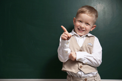 Photo of Funny little child near chalkboard, space for text. First time at school