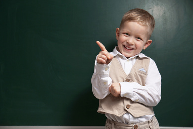 Funny little child near chalkboard, space for text. First time at school