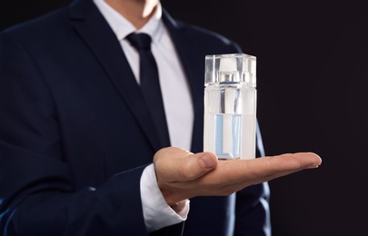 Photo of Young man with perfume bottle on black background, closeup