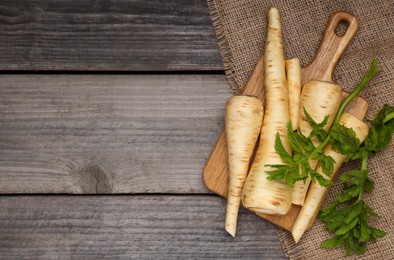 Photo of Many fresh ripe parsnips and green leaves on wooden table, flat lay. Space for text