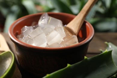 Aloe vera gel in bowl and slices of plant on wooden table, closeup