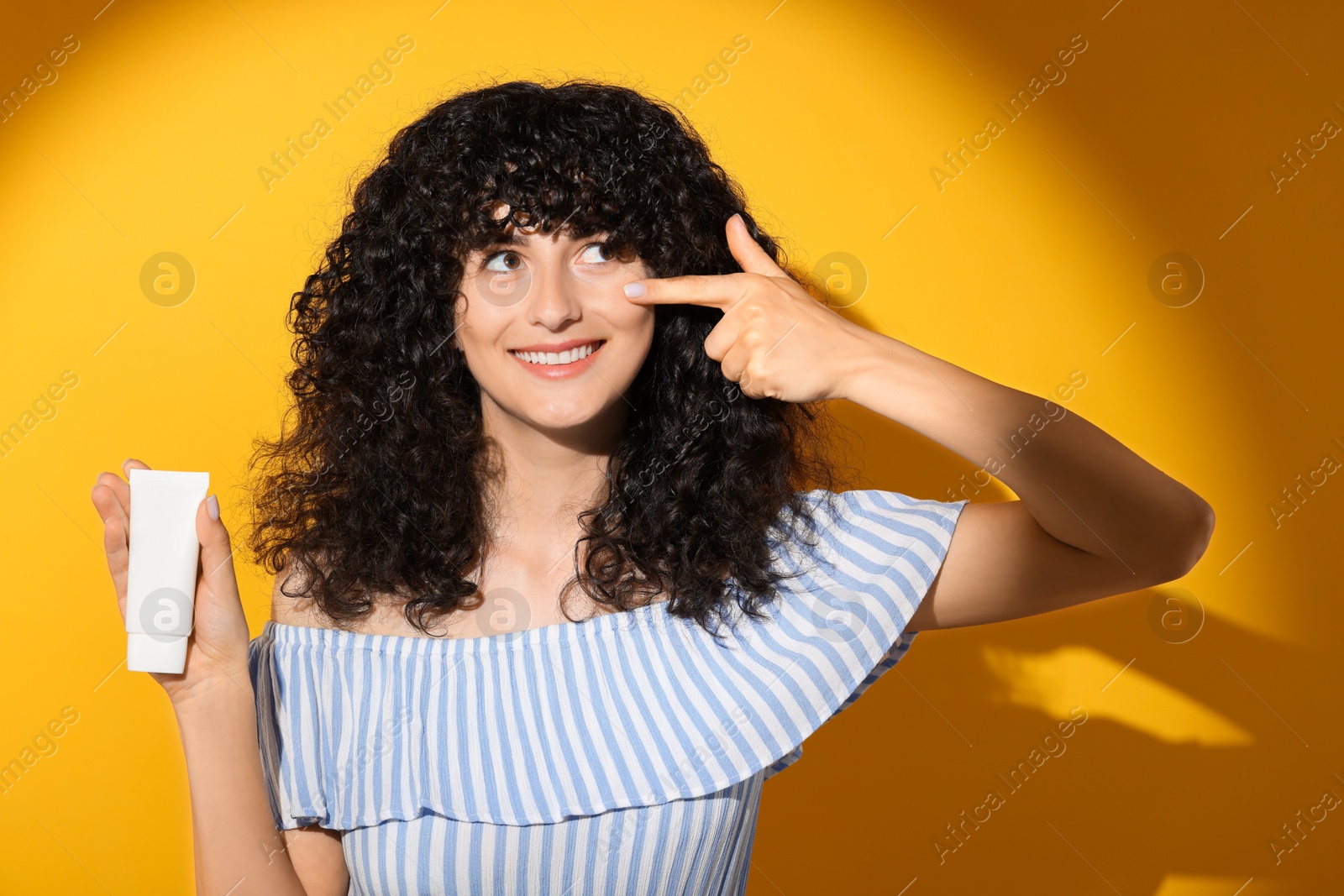 Photo of Beautiful young woman with tube of sunscreen in sunlight on orange background