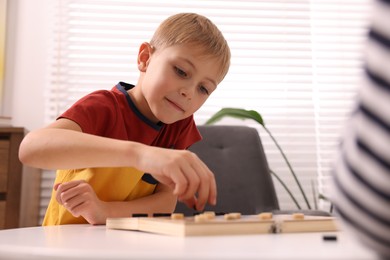 Cute boy playing checkers at coffee table indoors