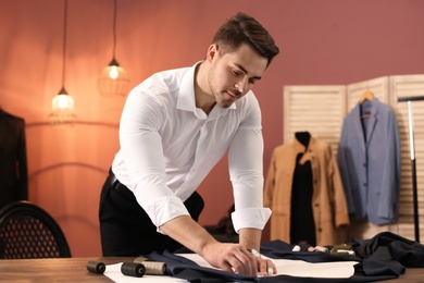 Photo of Young tailor working with sewing pattern in atelier