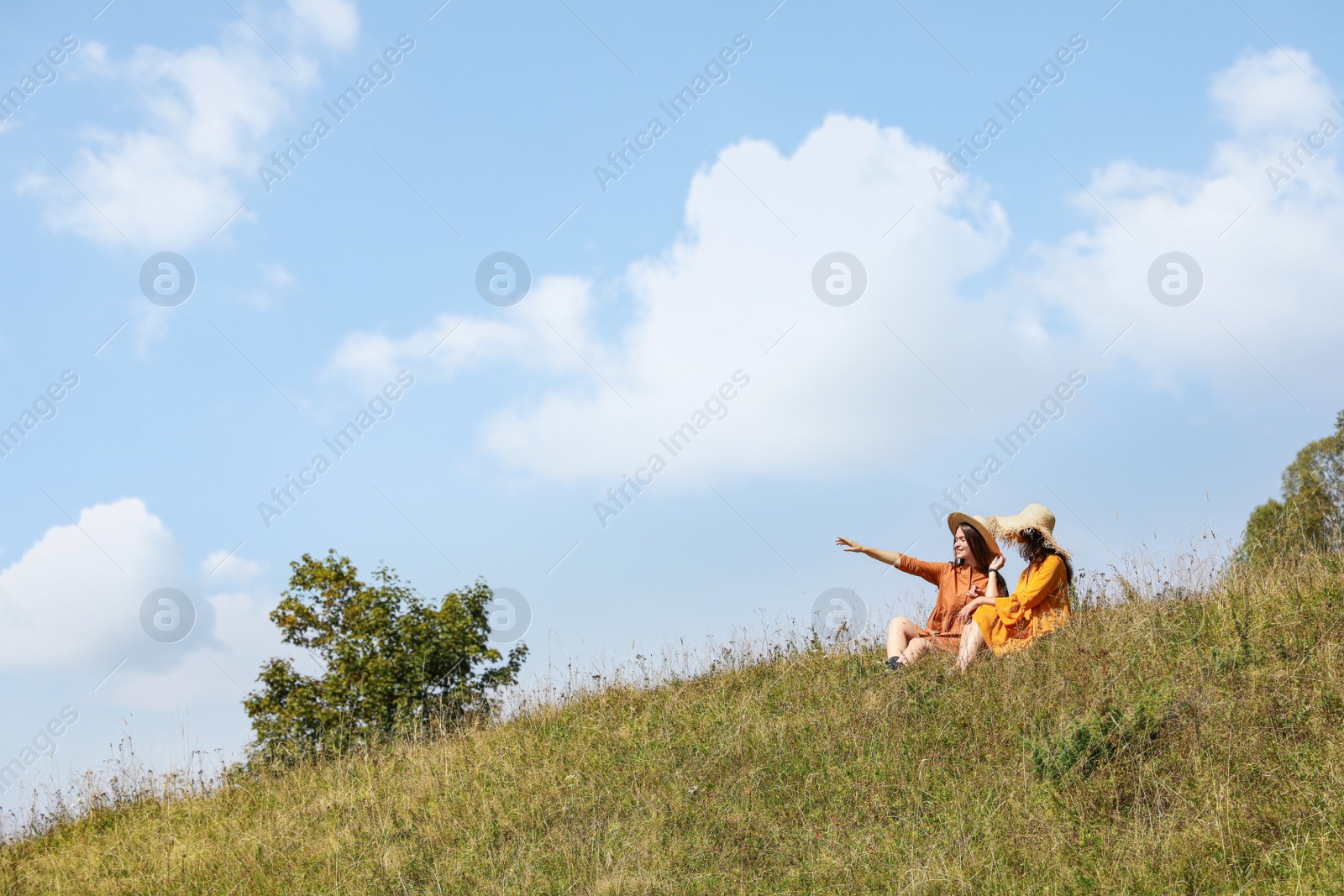 Photo of Women sitting on green hill outdoors, space for text