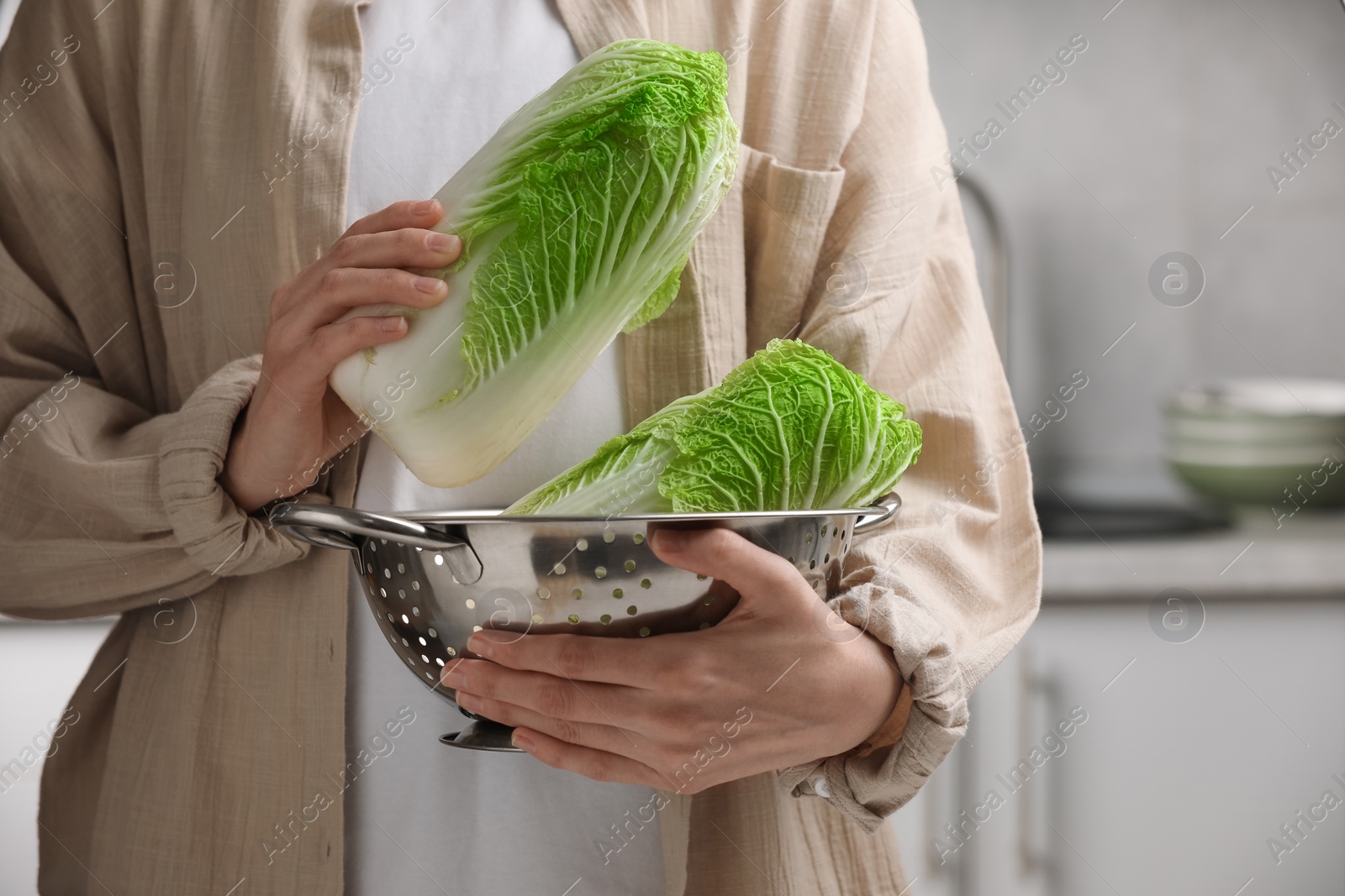 Photo of Woman holding fresh chinese cabbages in kitchen, closeup